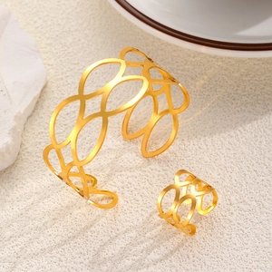 Detalle del conjunto de brazalete y anillo geométrico dorado sobre fondo texturizado