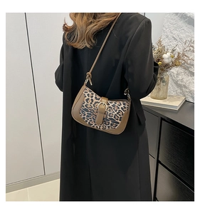 Model wearing a leopard print hobo bag with brown leather trim and metal buckle