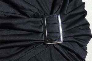 Detail of silver rectangular metal buckle on black pleated fabric with smooth texture