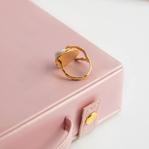 Détail d'une bague coeur en acier doré avec nacre posée sur un coffret à bijoux rose