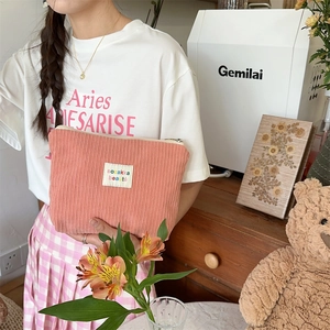Detail of pink corduroy makeup bag with woven logo label being held by a model