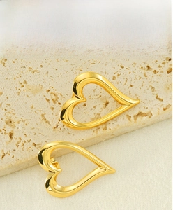 Detailed view of gold plated hollow heart studs on textured beige stone surface