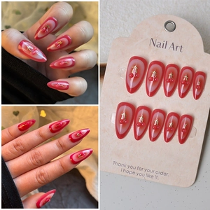 Macro detail of almond-shaped fake nails featuring red cherry charms and gold leaf accents