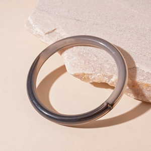 Detailed close-up of a smoke gray translucent acrylic bangle on a rough stone background