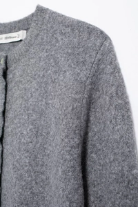 Close-up of grey knit cardigan featuring ruffled trim, round neck, and soft wool texture