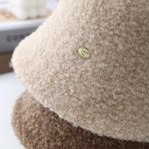 Minimalist beige teddy fleece bucket hat for women with a gold metal brand tag detail