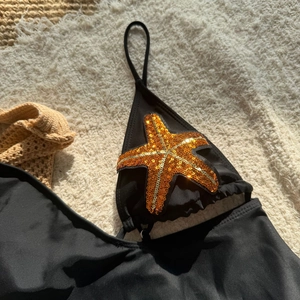 Detail of black swimsuit featuring a bright orange sequined starfish and thin straps