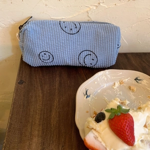 Detailed close-up of light blue corduroy cosmetic bag with black smiley face design