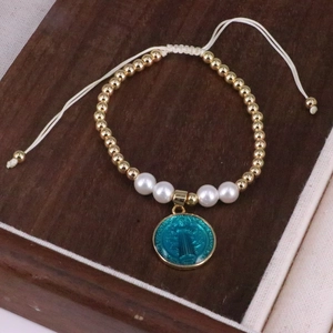 Macro detail of gold beads and blue religious charm on a handmade woven bracelet