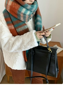 Close-up of thick plaid tassel scarf in orange and teal blue with white faux fur coat
