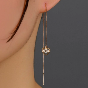 Detail of gold heart eye tassel earrings with shiny zircon on model in dark background