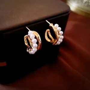 Double-layered gold C-shape pearl earrings displayed on a luxury leather jewelry box