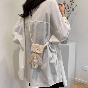 Minimalist beige woven crossbody bag with tassel detail on a white background
