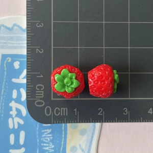 Dettaglio di mini ciondoli a fragola in resina con texture e scala di misura