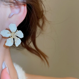 Close-up of silver flower stud earring with textured petals on a female model