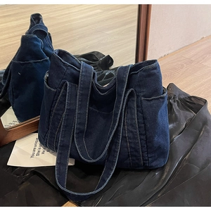 Detail view of large dark blue denim tote bag with dual straps on wooden floor