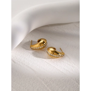 Detail of gold C-shaped hollow earrings with embedded white zircons on textured background