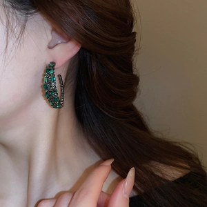 Detail of C-shaped emerald and grey crystal hoop earrings worn by a model