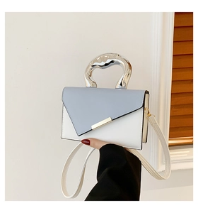 Detail of blue and white crossbody bag with curved silver metal handle and gold accents