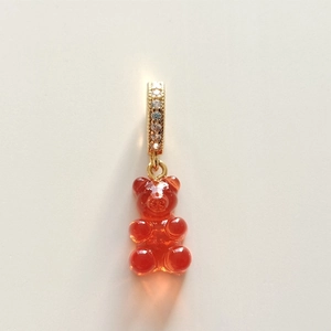 Macro view of red gummy bear pendant with gold diamond-encrusted loop on plain background