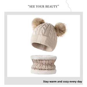 Detail of cable knit kids winter set featuring a beige beanie with faux fur double pom-poms
