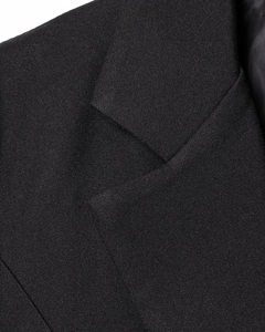 Detailed close-up showing the notch lapel and fine texture of the black blazer
