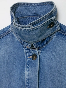Detail eines blauen Jeansjackenkragens mit dunklem Rundknopf und hochwertiger Naht