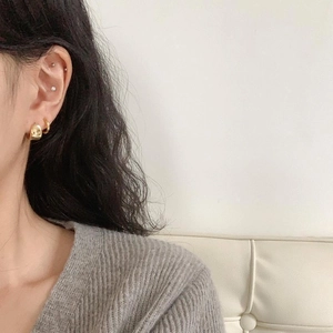 Close-up of minimalist gold oval hoop earrings worn on ear with a thick, sleek profile