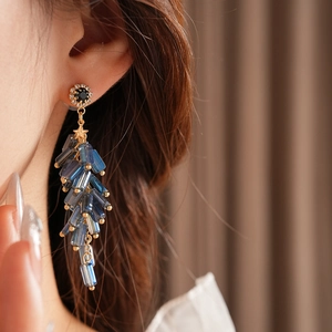 Detail showing blue beaded tassel earring with gold accents on model in soft lighting