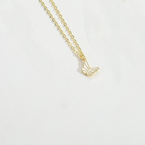 Detailed macro shot of a white butterfly pendant on a gold delicate necklace chain
