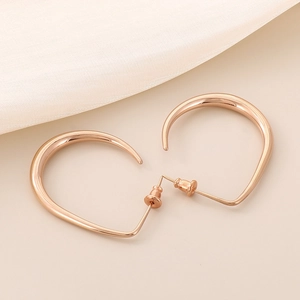 Detailed top view of rose gold U-shaped earrings on light beige fabric texture