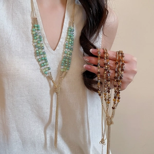 Detail of bohemian multilayered beaded necklace with long metallic tassel on model