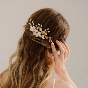 Detail of a bridal hair comb with gold leaves and white ceramic flowers on an elegant updo