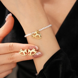 Close-up of pearl bracelet with golden rocking horse charm and matching earrings set