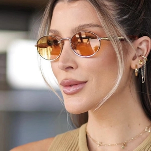Retro oval sunglasses with light orange lenses and gold frame on model with earrings