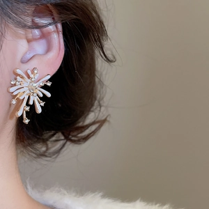 Close-up of golden firework-shaped stud earrings with zircon stones and enamel on the ear