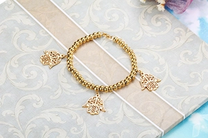 Macro detail of gold beaded stretch bracelet with three hollow Hamsa hand charms