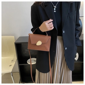 Detailed view of brown leather crossbody bag with unique gold geometric buckle and handle