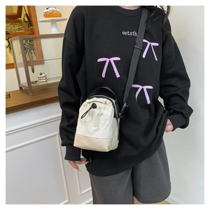 Model wearing a cream nylon drawstring crossbody bag with adjustable black strap