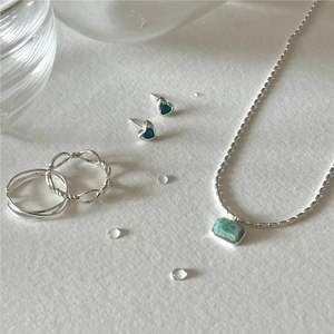 Detailed set of 925 silver jewelry with olive bead pendant and heart studs on white surface