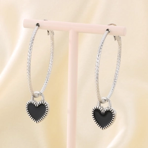Detail of silver hoop earrings with black enamel heart charms on a satin background