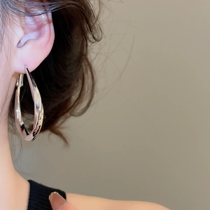 Close-up of twisted silver water drop hoop earring worn showing geometric metallic texture