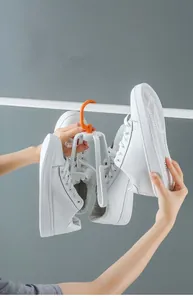 Detail of white shoe drying rack with orange hook showing non-slip arms and rotatable design