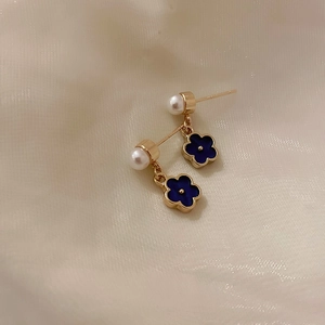 Detail of blue flower earrings with white pearls on a soft white silk background