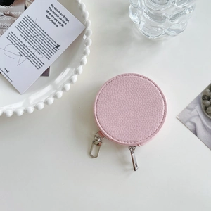 Detailed view of a round pink textured leather coin purse with silver zipper on a white table