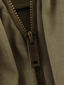 Détail macro de la fermeture éclair en bronze antique sur un blouson bomber vert olive