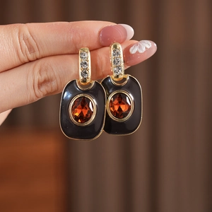 Detail of vintage gold earrings with black enamel and an orange gemstone held by hand
