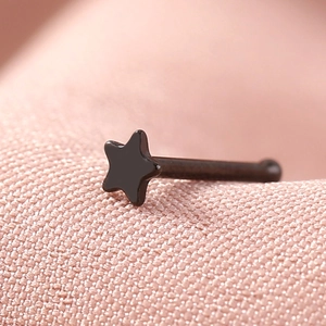 Macro shot of a black star-shaped stainless steel nose stud on a soft pink background