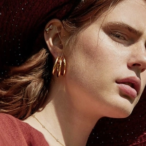 Détail macro de boucles d'oreilles créoles triples dorées portées par un mannequin poli