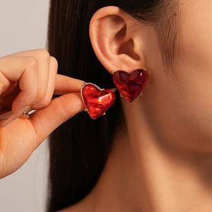 Close-up of red heart resin earring with gold metal trim worn on ear for detail